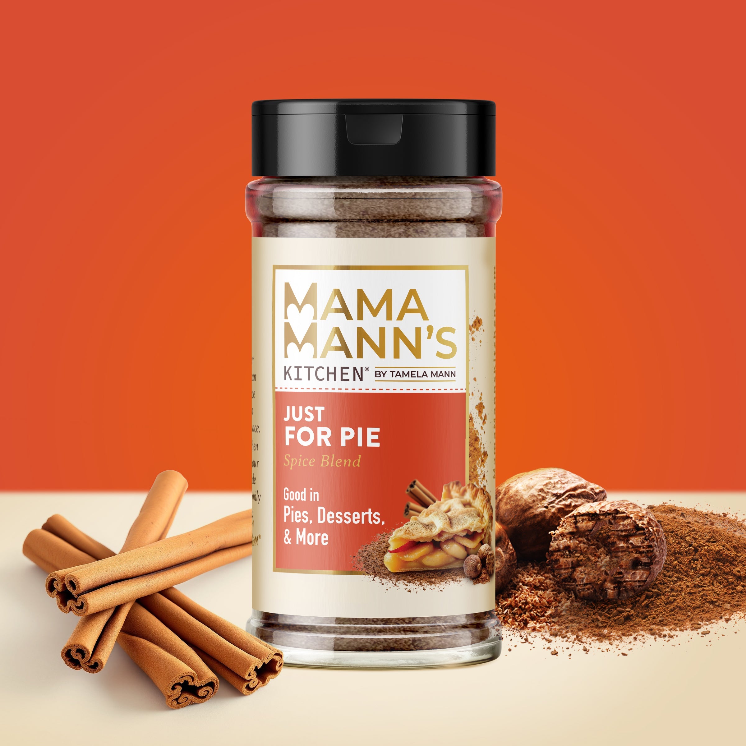 Mama Mann's Kitchen spice blend jar with cinnamon sticks and a pie on an orange background